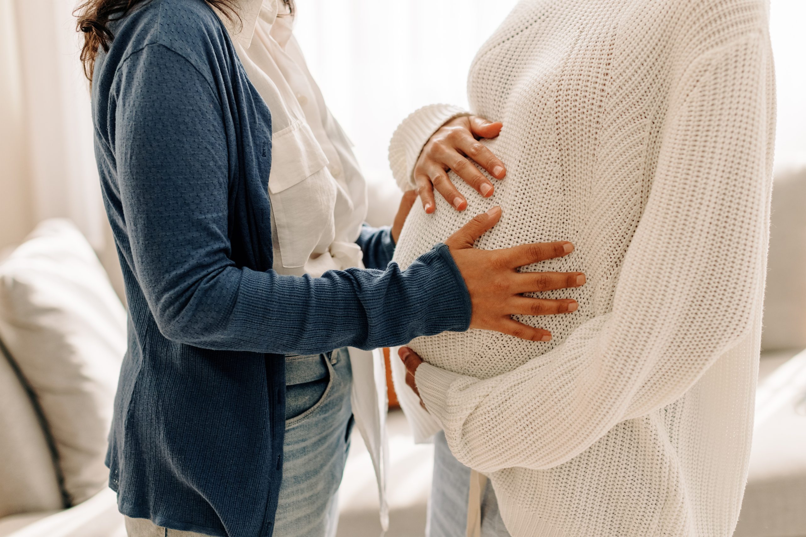Unrecognizable young woman touching her surrogate's pregnant bel hugging